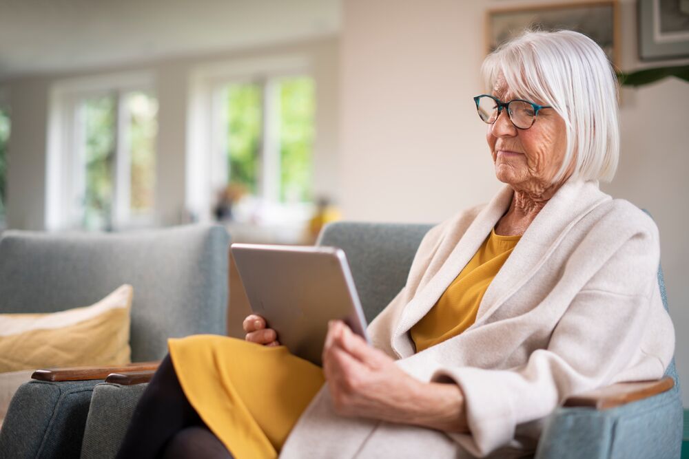 Oudere vrouw zit op bank met tablet