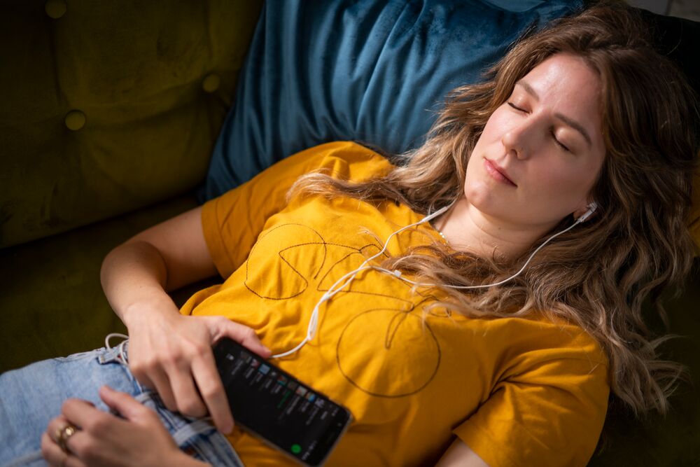 Jonge vrouw luistert muziek via telefoon op bed