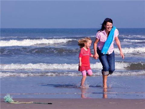 Moeder en dochter lopen met blote voeten in de branding, op het strand
