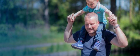 Vader en zoon lopen buiten, zoon zit op de nek van zijn vader