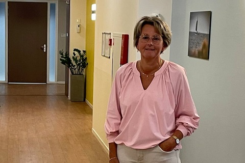 vrouw staat in de gang van een zorginstelling en kijkt in de camera