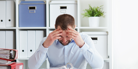 man zit in een kantooromgeving met handen aan zijn hoofd