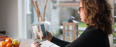 Vrouw aan keukentafel in gesprek met persoon via tablet