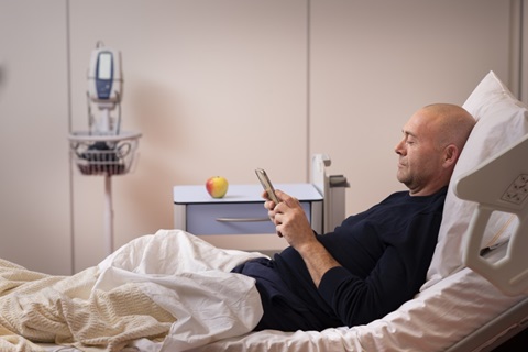 Man in ziekenhuisbed kijkt op telefoon